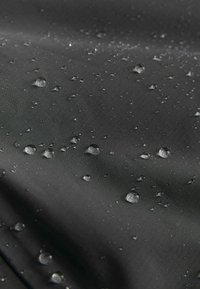 Sort stof med en glat tekstur, prydet med vanddråber spredt over overfladen, hvilket fremhæver dets vandafvisende egenskaber.