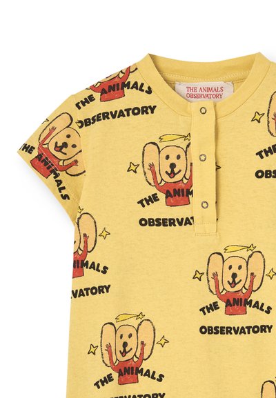 Sárga pamut póló, nyomtatott rajzfilm kutya mintákkal és a "THE ANIMALS OBSERVATORY" felirattal feketében. Gombos gallérral rendelkezik.