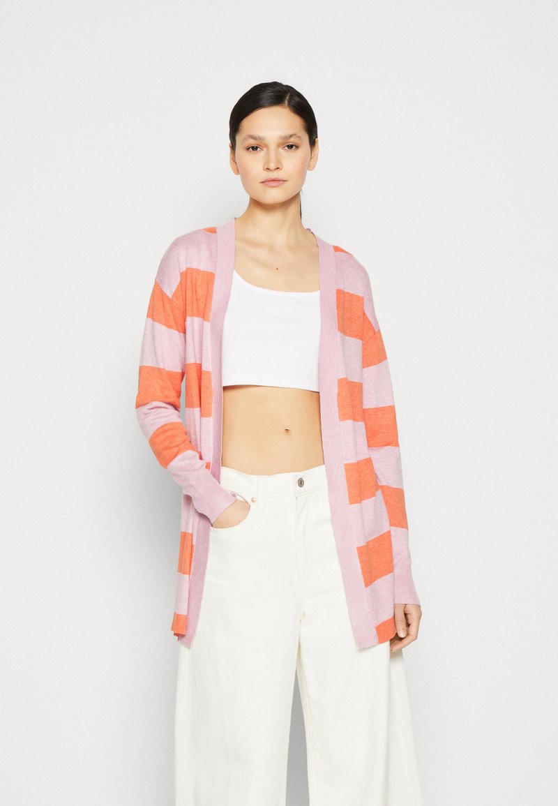 Rosa och orange randig cardigan, öppen fram, lång ärm, lätt stickad kvalitet, kombinerad med en vit crop top och krämfärgade vida byxor.