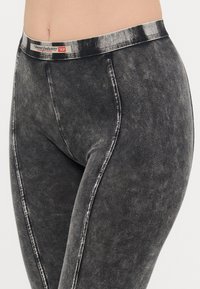 Černé denim legíny mají texturovaný povrch s vybledlým vzhledem. Temný pás zobrazuje logo "Diesel Industry" v kontrastních barvách.