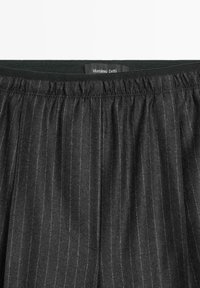 Zwarte broeken met een streepmotief, elastische tailleband en een label met "Massimo Dutti." De stof lijkt textuur te hebben.