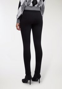 Leggings nere in tessuto elasticizzato, con vita alta e texture liscia, abbinate a stivaletti neri con tacco alla caviglia.