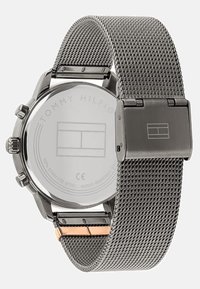 Montre en acier inoxydable avec un bracelet en maille, dotée d'un boîtier rond et d'un dos lisse argenté avec un logo gravé. Comprend un accent doré sur le fermoir.