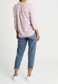 Camicia a righe rosa chiaro e bianca con maniche a tre quarti, abbinata a jeans blu denim risvoltati e sneakers bianche.