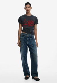 Grafisches graues T-Shirt mit rot bedrucktem "LOVE"-Schriftzug, kombiniert mit lockeren blauen Denim-Jeans mit fünf Taschen und kontrastierenden Nähten.