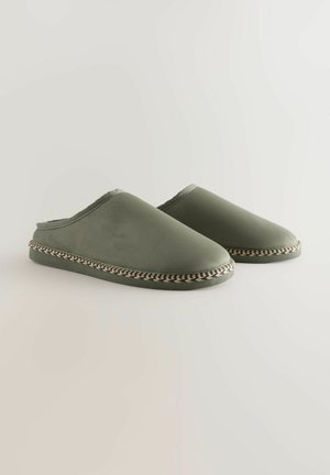 Gröna slip-on tofflor med en slät textur, med en vävd kant i svart och beige runt sulan, samt en öppen baksida.