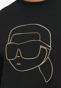 Arte lineare minimalista in oro di una persona con grandi occhiali da sole e capelli raccolti su uno sfondo di tessuto nero.