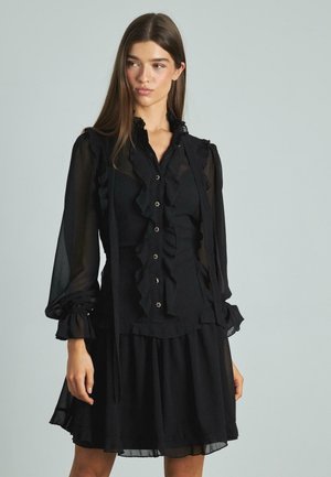 Schwarzes Kleid mit langen, transparenten Ärmeln, Rüschenausschnitt und Frontleiste mit Knöpfen. Weicher Stoff und schichtendes Design.
