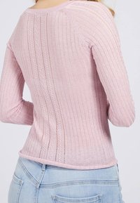 Maglione rosa chiaro a coste con maniche lunghe, caratterizzato da strisce orizzontali e verticali e un orlo leggermente curvo. Tessuto a maglia morbido.
