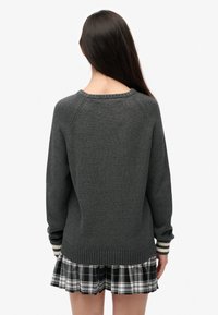 Szary sweter z dzianiny z okrągłym dekoltem i ściągaczami przy mankietach, zestawiony z czarno-białą spódnicą w kratę z falbaną na dole.