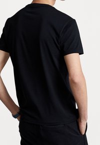 Černé bavlněné tričko s krátkým rukávem, kulatým výstřihem a hladkou texturou. Střih je ležérní s minimem švů, nošeno s černými kalhotami.