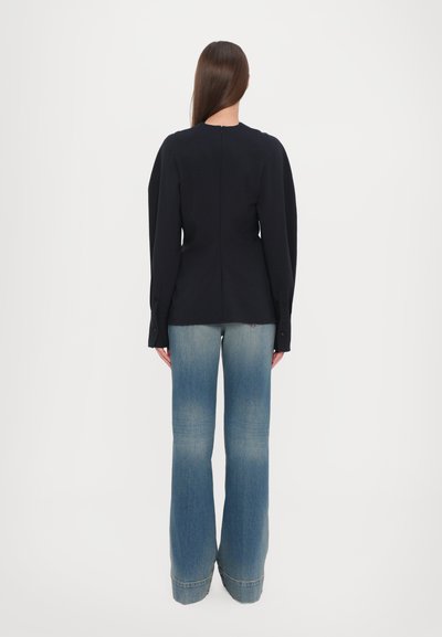 Marineblå langærmet top med rund halsudskæring og knappede manchetter, parret med lyseblå bootcut jeans, der viser en glat denimtekstur.