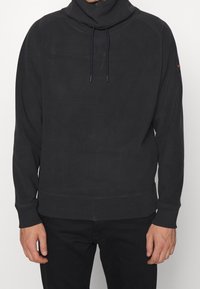 Sudadera negra con cuello alto, detalles de cordón y puños y dobladillo acanalados. Tela suave con un ajuste relajado.