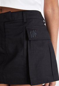 Črna plisejska krila iz lahkega materiala, z stransko žepono in izvezenim logotipom ter prilegnjenim pasom.