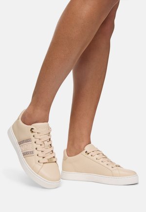 Beige Sneakers mit einem glatten Leder-Obermaterial, goldenen Beschlägen, einem dekorativen Streifenmuster und einer weißen Gummisohle.