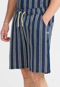 Marineblå shorts med hvide lodrette striber, udstyret med elastisk talje, snor og sidelommer. Stoffet har en tekstureret overflade.