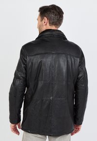 Zwarte leren jas met een gestructureerde afwerking, met een brede kraag en een gequilt patchwork ontwerp. Goed zichtbare stiksels overal.