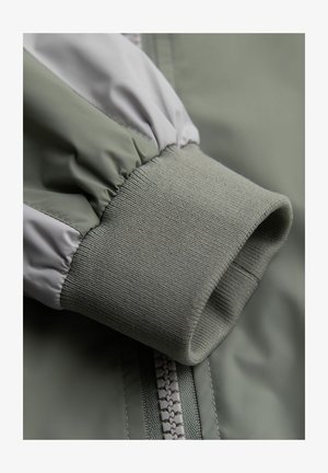 Grøn jakkeærme med elastiske manchetter og et glat, skinnende stof. Inkluderer en kontrasterende grå detalje nær skulderen.