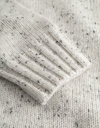 Hellgrauer, gestrickter Pulloverstoff mit gesprenkelten schwarzen Akzenten. Verfügt über gerippte Bündchen und eine weiche, strukturierten Oberfläche. Nahaufnahme.