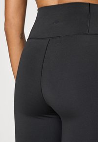 Höga svarta leggings av elastiskt tyg, med en slät yta och subtila detaljer vid midjan.