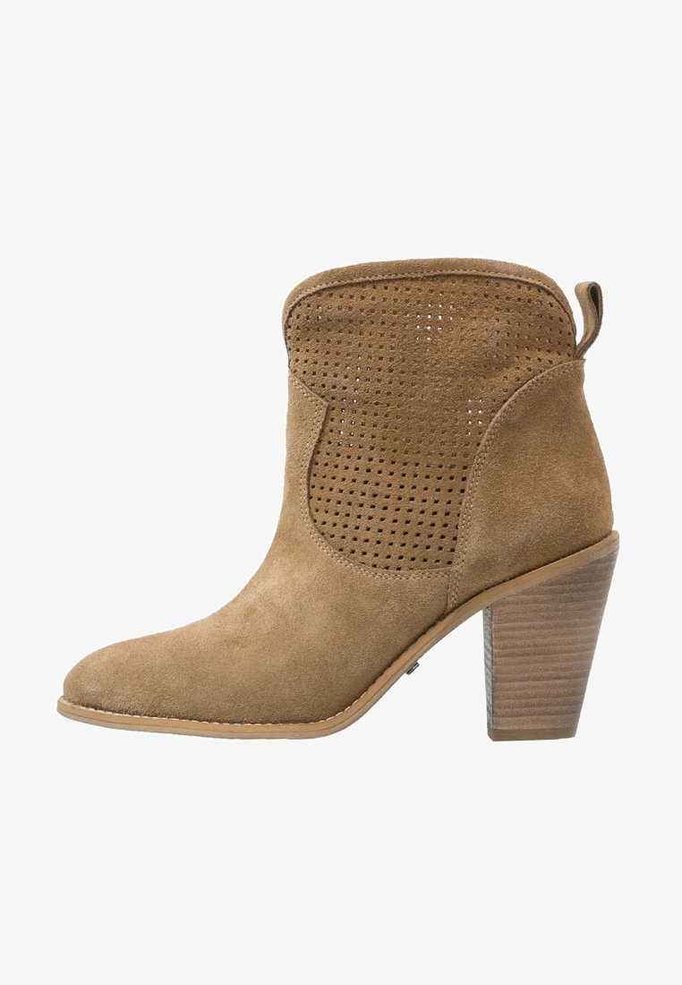 Stivale alla caviglia in suede marrone con design perforato, punta affilata e tacco impilato. Finitura senza giunture con una linguetta sul retro per indossarlo facilmente.