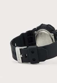 Čierny gumený remienok G-SHOCK so striebornou kovovou sponou. Obsahuje textúrované akcenty a odolný, flexibilný dizajn.