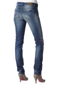 Smal blå denimjeans med en urtvättad finish, två bakfickor och en brun läderetikett på midjan. I kombination med grå höga klackar.