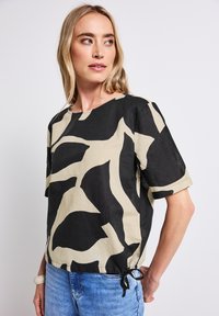 Černo-beige vzorované tričko s krátkým rukávem, které má volný střih a zavázání na boku, vyrobené z lehkého materiálu.