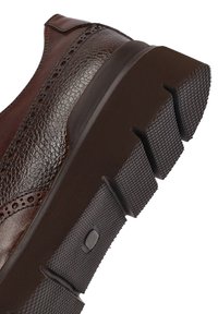 Semelle de chaussure en cuir marron avec de profonds sillons et un crantage en caoutchouc texturé pour une meilleure adhérence et durabilité.