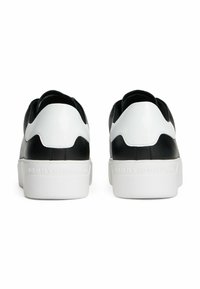 Ein Paar schwarze und weiße Low-Top-Sneaker von hinten betrachtet, mit "Tommy Hilfiger" auf den weißen dicken Sohlen eingeprägt.