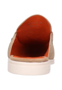 Tan suède instapschoen met een witte zool, voorzien van een feloranje interieur en kleine decoratieve accenten. Open hielontwerp.