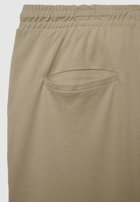 Beige Hose aus strukturiertem Stoff, mit elastischem Bund und einer aufgesetzten Tasche an der Seite.