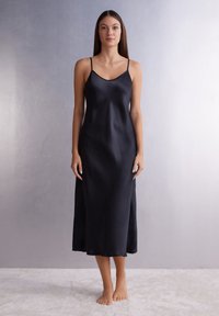 Vestido de satén negro tipo slip con tirantes finos, escote redondeado y una silueta A-line que llega hasta la mitad de la pantorrilla. Textura suave.