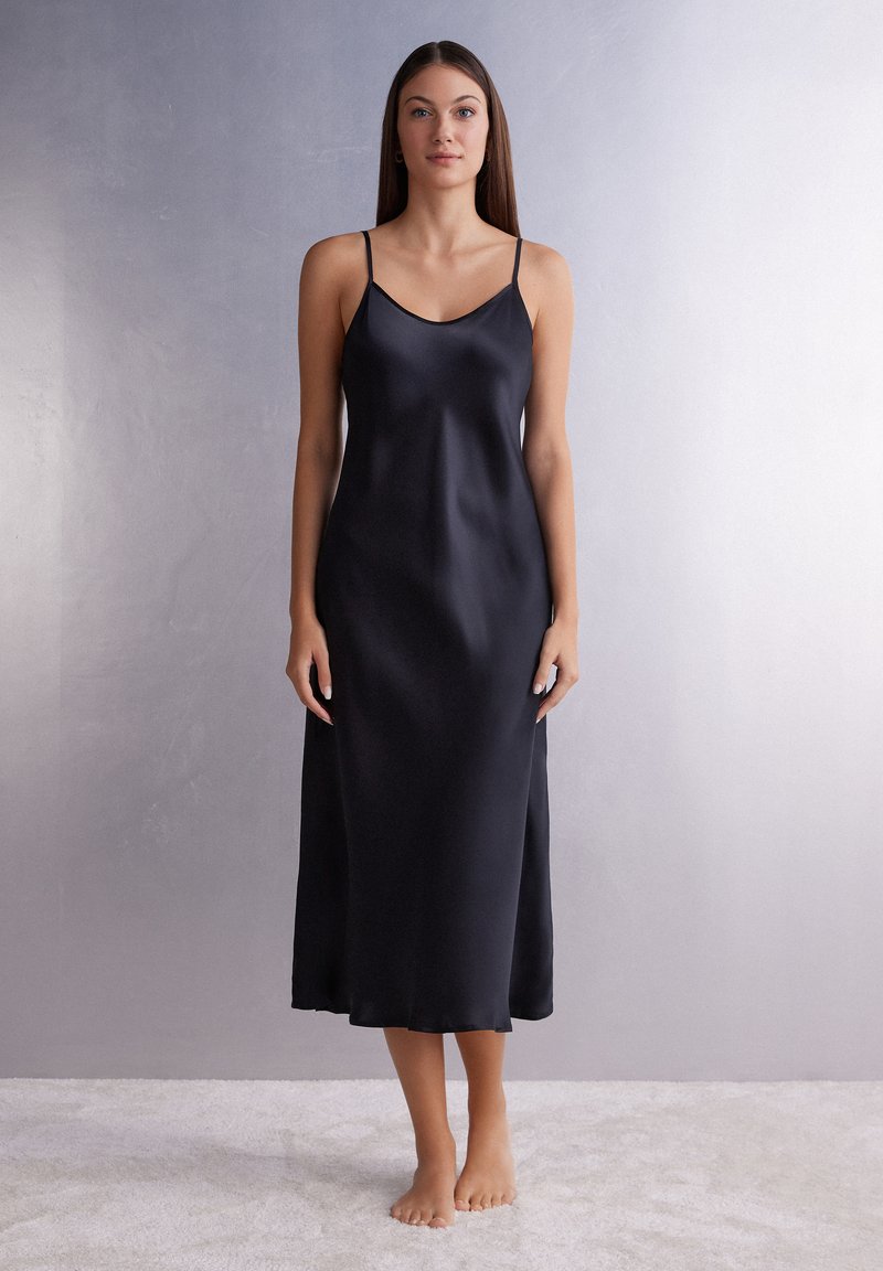 Vestido de satén negro tipo slip con tirantes finos, escote redondeado y una silueta A-line que llega hasta la mitad de la pantorrilla. Textura suave.