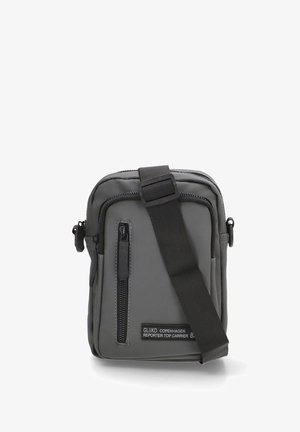 Bolso de hombro gris hecho de tela duradera; cuenta con un bolsillo frontal con cremallera, correa ajustable y parche con logo. Diseño rectangular compacto.