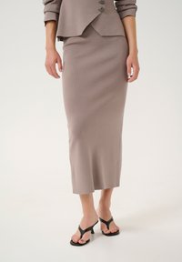 Helle taupe-rippstrick-Umstandsröcke kombiniert mit einem passenden, taillierten Blazer. Das Outfit zeichnet sich durch eine klare Silhouette und Knöpfe am Blazer aus. Schwarze, hohe Flip-Flops.