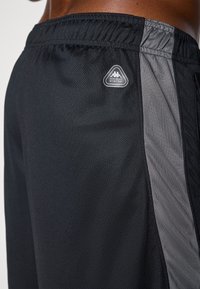 Svart treningsshorts laget av nettingmateriale med en grå sidestykke. Har et elastisk midjebånd og et trekantet logo-patch.