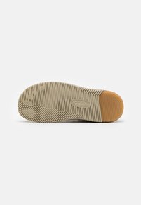 Schuhsohle mit beigem geripptem Profil, orangefarbener Fersenteil und dem eingeprägten KEEN-Logo in der Mitte.