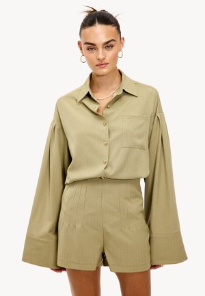 Chemise olive verte à boutons avec des manches oversized, poche avant et légères rayures; associée à un short plissé assorti.