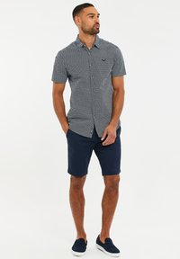 Korte ærmer, marineblå mønstret skjorte med knaplukning, parret med marineblå shorts og mørke slip-on sko.