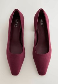 Décolleté in suede bordeaux con punta quadrata, texture liscia e soletta imbottita. Caratterizzato da un design minimalista senza hardware visibile.