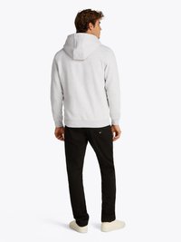 Grå hettegenser laget av myk stoff, båret med svarte bukser og hvite sneakers. Designet har en kengurulomme og ribbestrikkede mansjetter.