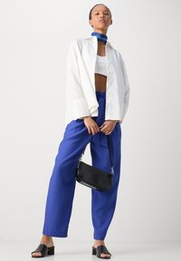 Bílé oversized tričko, modré široké kalhoty s uvázaným pasem, černá kabelka a černé sandály na blokovém podpatku. Hladké textury látky.
