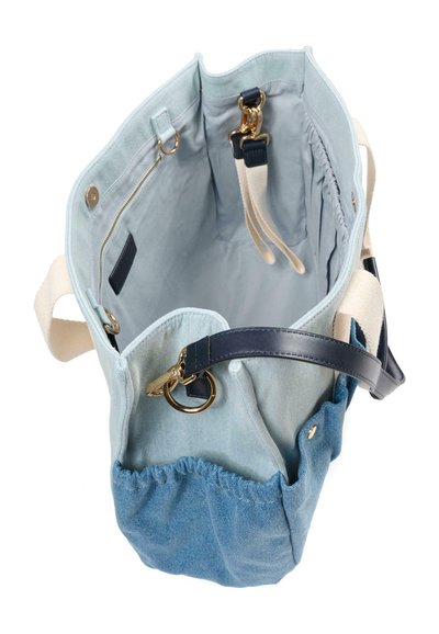 Lichtblauwe denim tote bag met beige handvatten, donkerblauwe leren riemen, gouden hardware en een binnenritssluiting en elastische zakken.