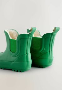 Bottes en caoutchouc vertes avec doublure douce et duveteuse, présentant un talon surélevé, des semelles texturées et des panneaux élastiques latéraux pour un enfilage facile.