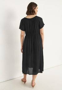 Schwarzes, knielanges Kleid mit kurzen Ärmeln, einem gerafften Oberteil und einem fließenden Rock. Leichte Textur, weicher Stoff und schlichte Silhouette.
