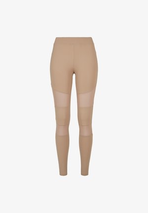 Bežid leggingsid, millel on sile tekstuur, sisaldavad võrkpaneele reitel ja sääremikes hingavuse ja sobiva disaini tagamiseks.