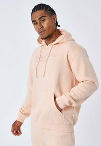 Perzikkleurige hoodie met een voorzak, trekkoorden en geborduurd "PROJECT X" logo. Zachte katoenmix met ribgebreide manchetten.