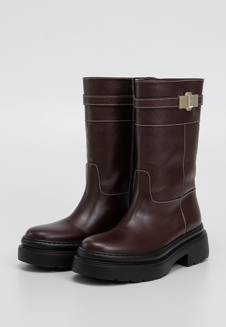 Dunkelbraune Lederstiefel bis zur Mitte der Wade mit schwarzen klobigen Sohlen, weißen Nähten und einem goldenen Schnallenriemen-Detail nahe der Oberseite.