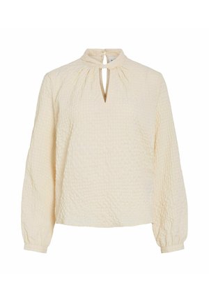 Krämsfärgad blus med en texturerad yta, långa ärmar, en nyckelhålöppning vid halsen och en veckad design vid axlarna.